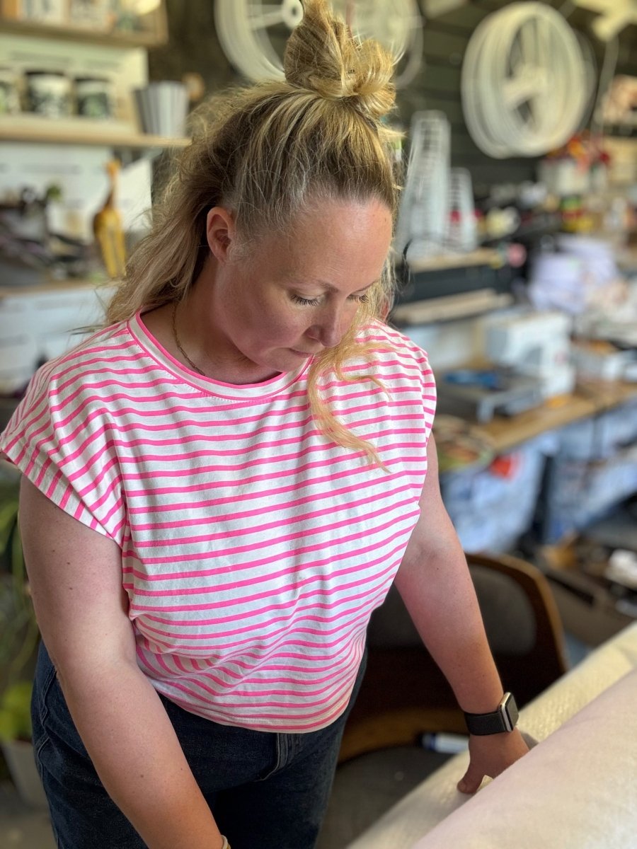 Zoe, founder of Mustard & Gray Studio, working at a table in the light-filled Shropshire studio. Surrounded by shelves of tools, designs, and creative materials, she focuses on her process of bringing contemporary homeware and stationery to life.