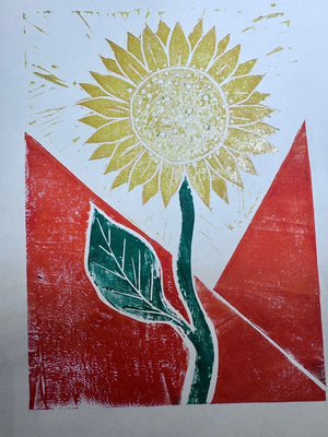 Colourful jigsaw linocut print of a sunflower with a yellow flower, green stem and leaf, and bold red background.