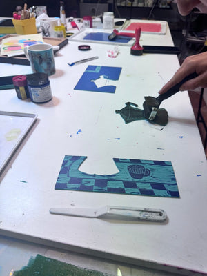 Jigsaw linocut blocks being individually inked with a roller during a multi-colour printmaking workshop.