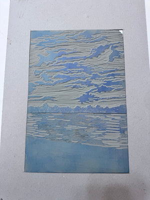 Carved jigsaw linoblock of a coastal landscape with sea and dramatic clouds, ready to be inked and printed.