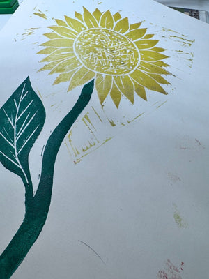 Two-colour jigsaw linocut print of a sunflower with a yellow flower head and deep green stem and leaf.