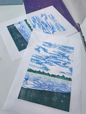 Multi-colour jigsaw linocut prints of a coastal landscape, with blue water and sky and a dark green shoreline.