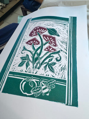 Two-colour jigsaw linocut print featuring stylised mushrooms, leaves and bees in green and burgundy.