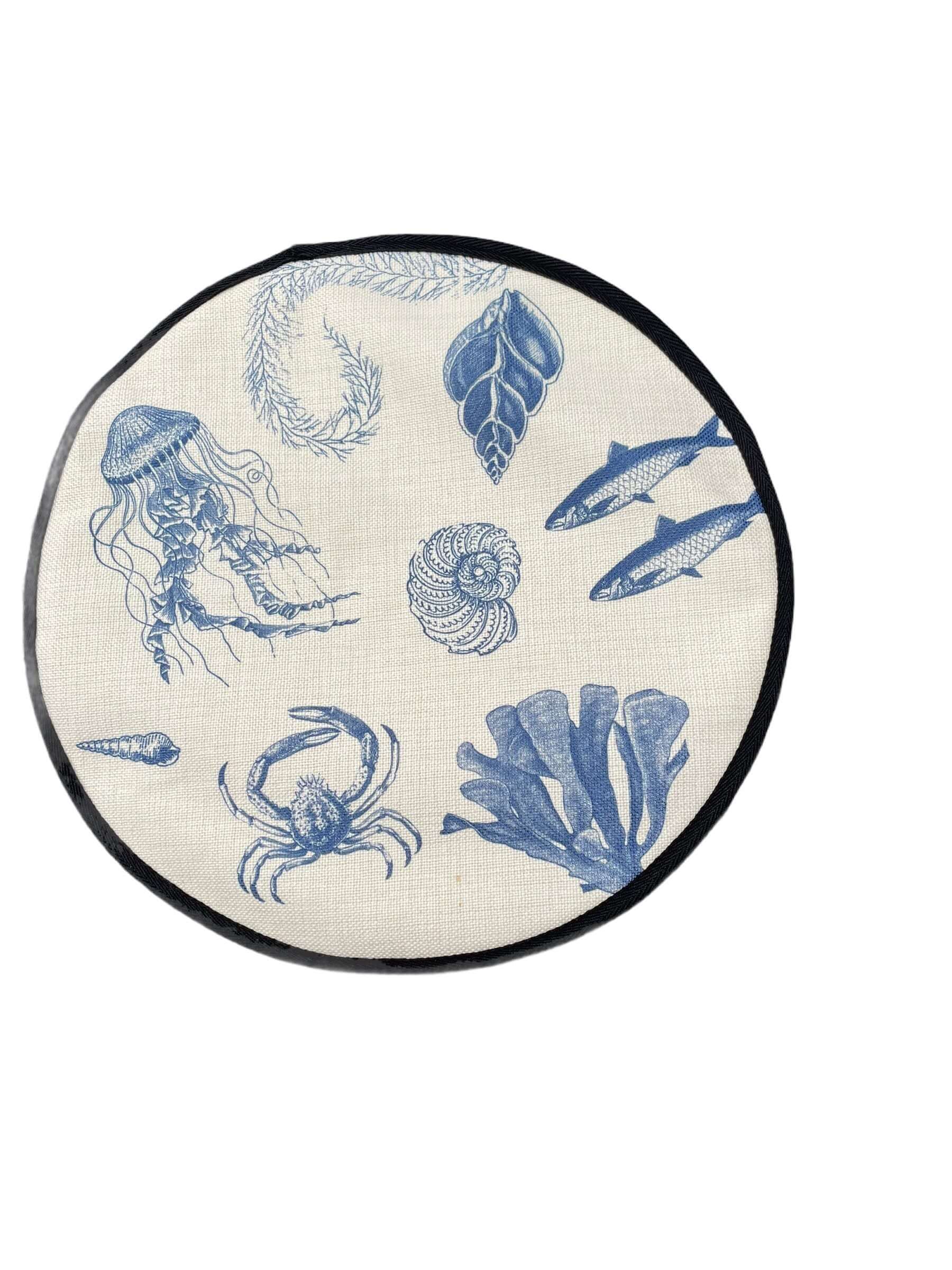 blue illustrations of sealife including fish, seaweed, shells, crabs, jelly fish, and fossilson a beige linen circular hob cover with black hemming.  Mustard and Gray
