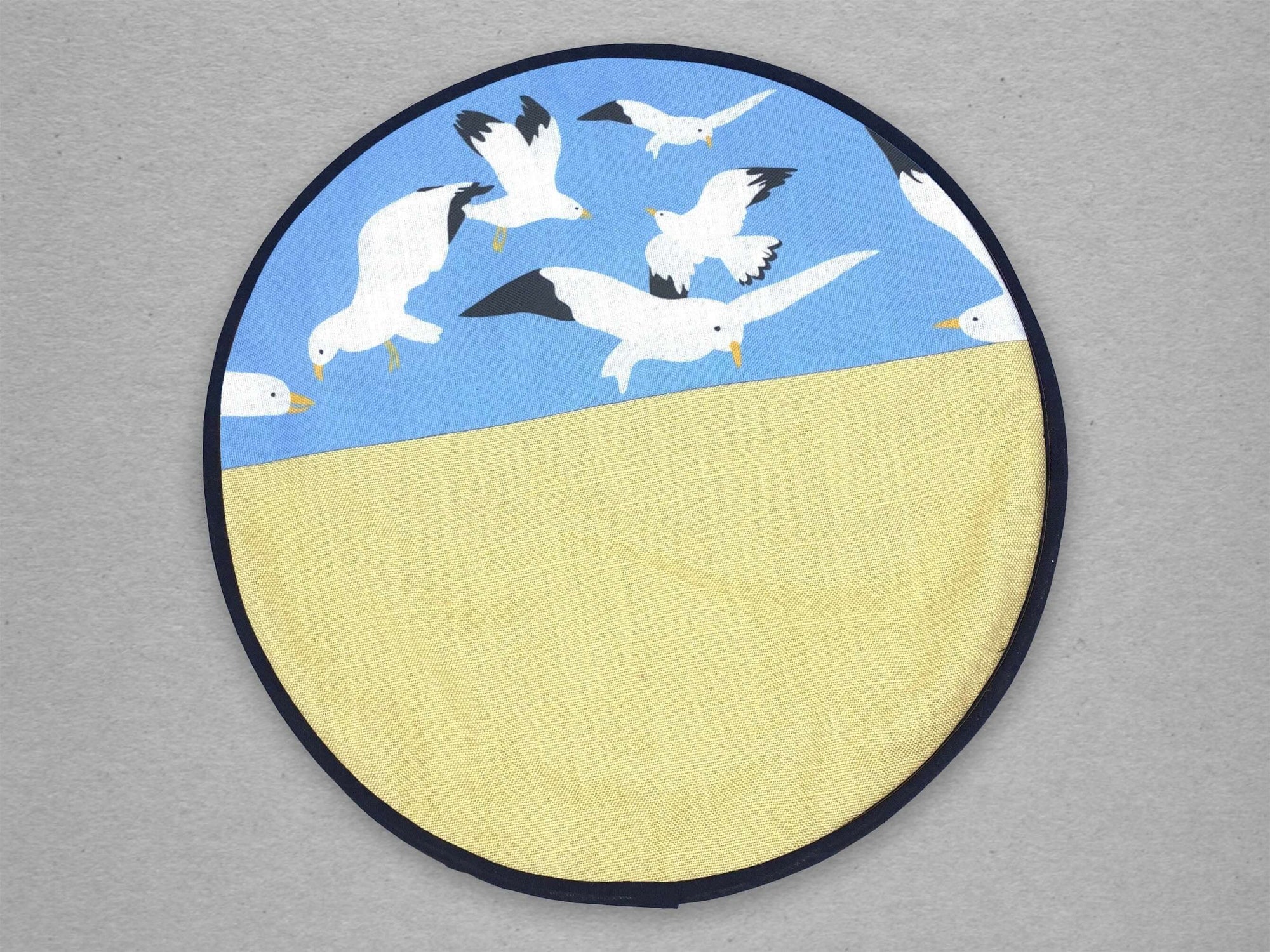 Circular design with seagulls flying on a bright blue background above yellow representing sand. .Oh Gully hob cover cooker Accessories Mustard and Gray Ltd Shropshire UK