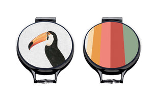 Set of two hob covers. Toco Toucan illustration print on a beige linen circular aga cover with black hemming. Stripes of Green, red, Pink and orange on one hob cover and fish tail of the other hob cover. Pictured on metal cooker lid on an isolated background. Mustard and Gray